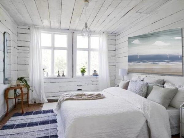 Coastal-style bedroom with a seascape painting above a white bed.