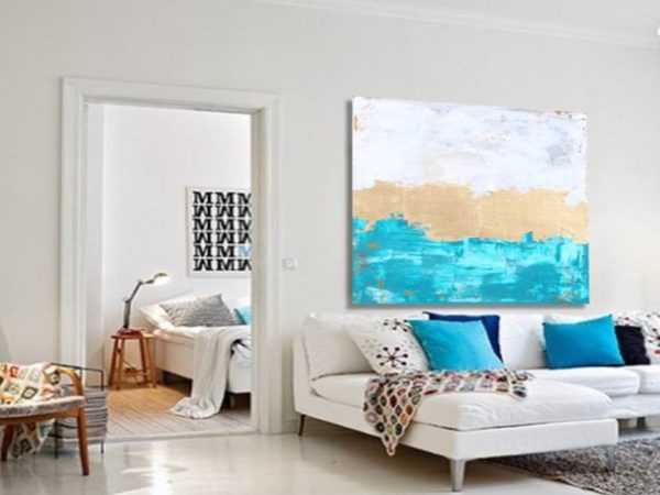 Gold abstract painting above white sofa in a bright modern living room.