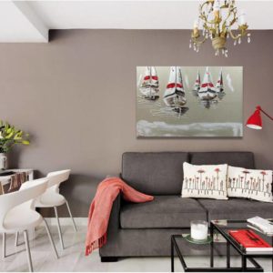 Seascape painting with white sailboats above a gray sofa.