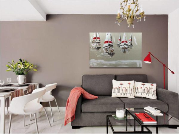 Seascape painting with white sailboats above a gray sofa.